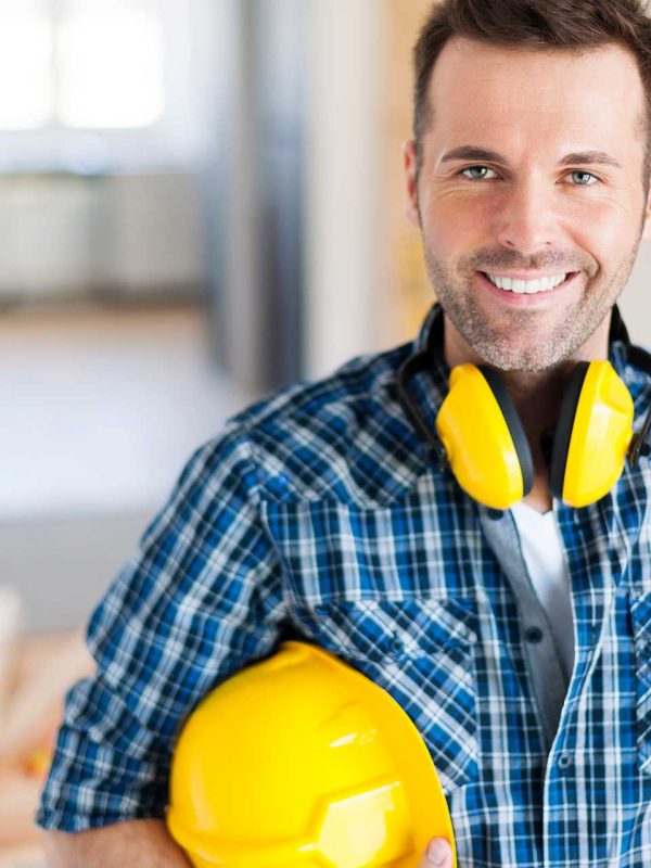 Smiling construction worker with yellow helmet and ear protection.